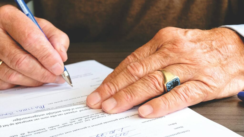pexels-photo-618158-618158 Close-up of a senior adult signing a legal document with a focus on hand and gold ring., thanadoula doula accompagnement soutien deuil familles fin de vie.