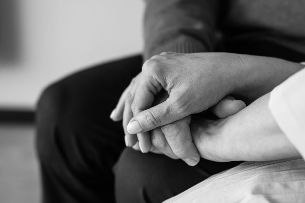 pexels-photo-8057349-8057349 Black and white image of two hands holding, conveying comfort and support, close-up view, thanadoula doula accompagnement soutien deuil familles fin de vie.