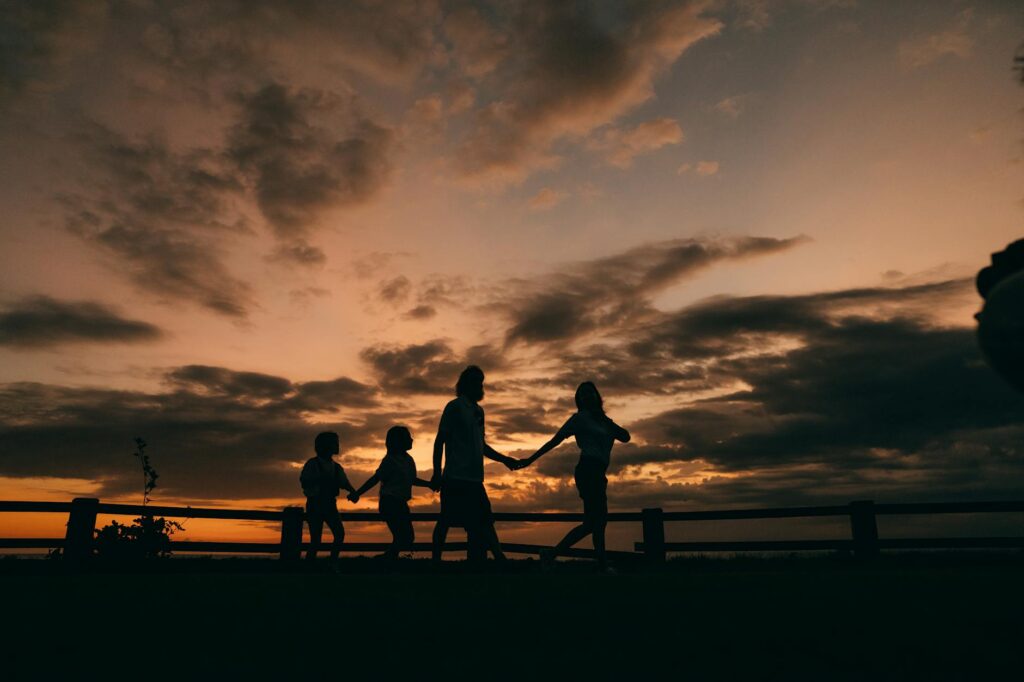 pexels-photo-9207532-9207532 A family holding hands and walking in silhouette against a stunning sunset sky, thanadoula doula accompagnement soutien deuil familles fin de vie.